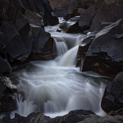 A long-exposure river flowing as white mist between dark wet rocks
